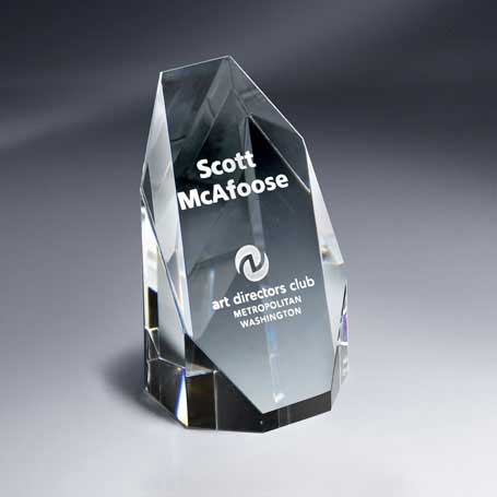 An optic crystal silhouette tower award with engraved text, placed on a gray surface.