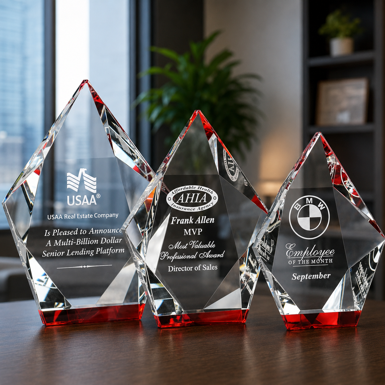 Three faceted crystal award plaques with red-tinted bases in an office setting. The plaques are engraved with company and individual awards.
