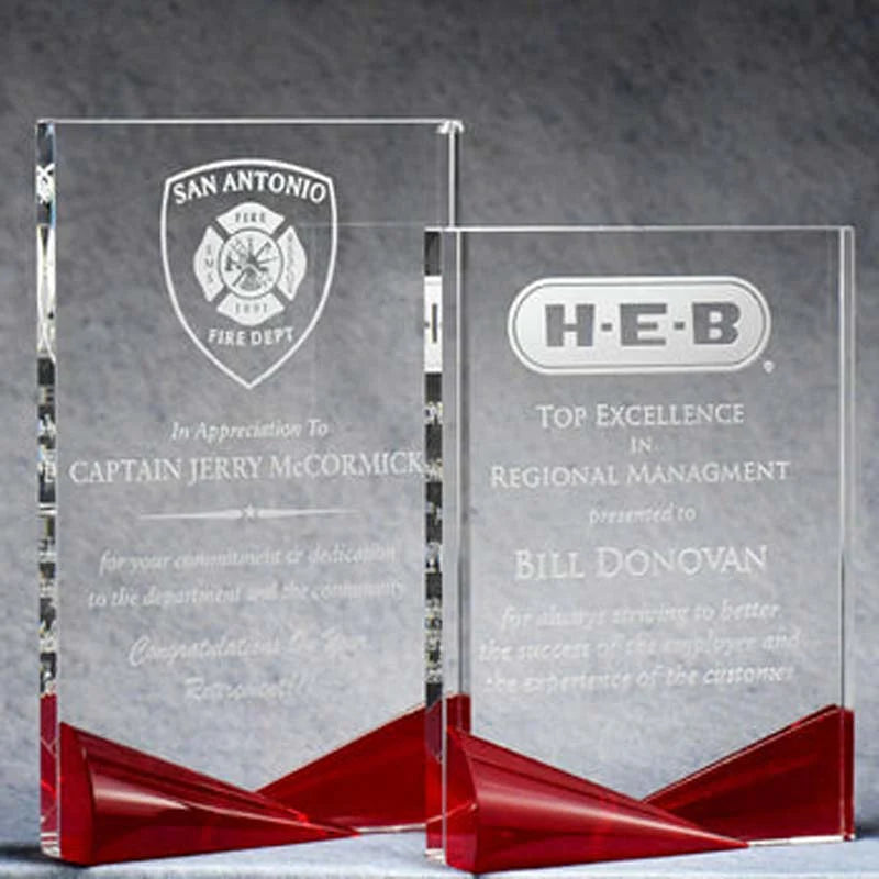 Two crystal award trophies with red bases and etched engravings. One trophy is smaller and presented in front of a larger trophy.