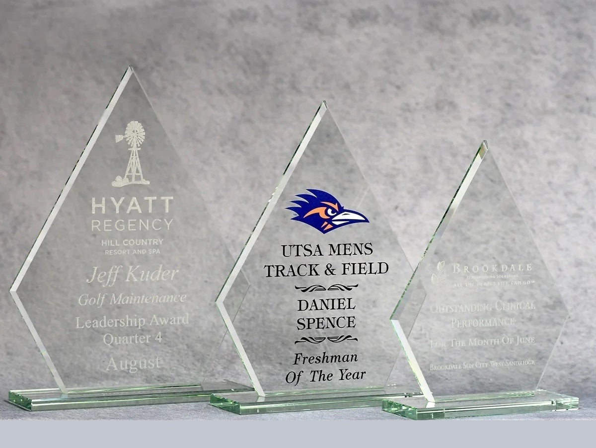 Three glass awards with engraved text on a gray background