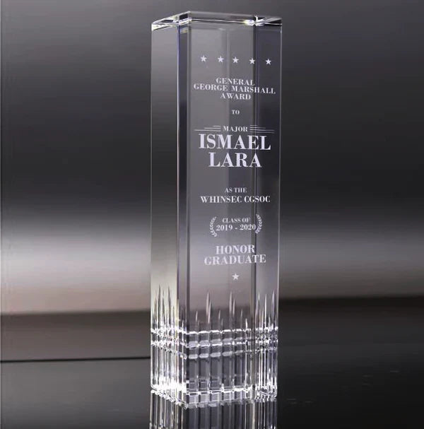 Tall, clear glass award with engraved text on a dark background
