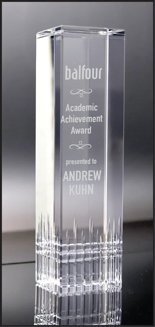 Clear glass award with engraved text on a reflective surface