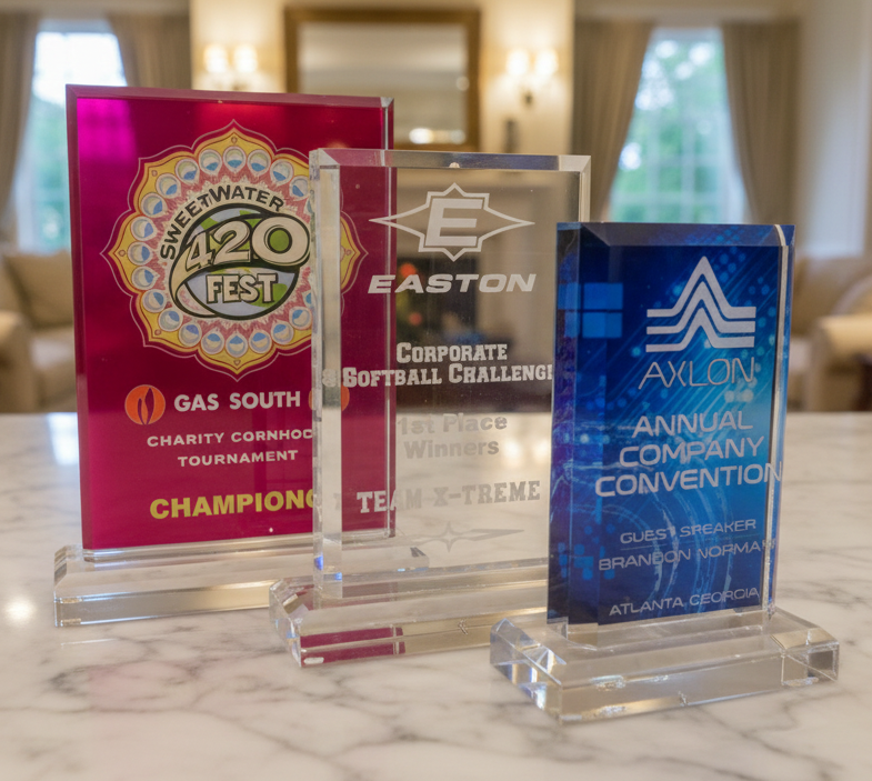Three clear acrylic awards with colorful designs on a marble surface.