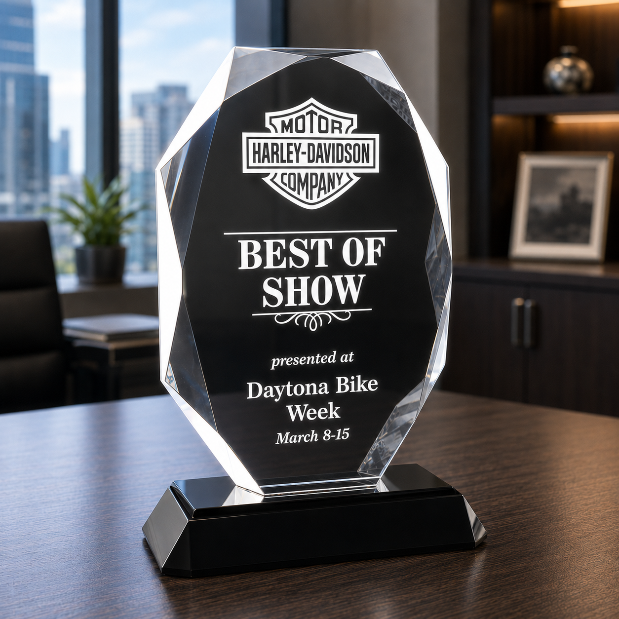 A faceted clear acrylic award plaque on a black base, engraved with a logo and the text, displayed in an office setting.
