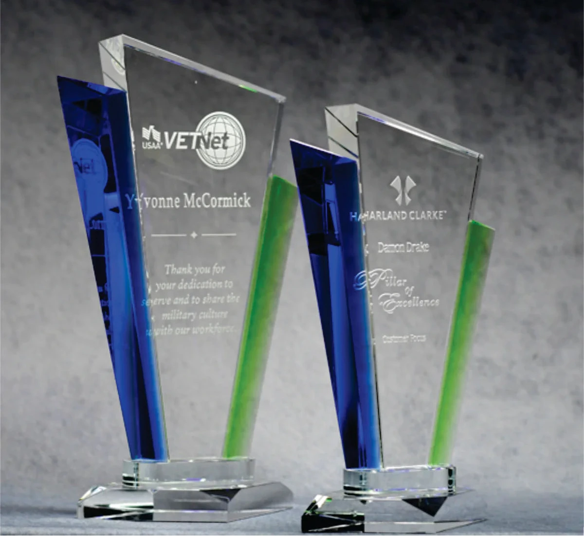 Two optic crystal palace awards with blue and green accents, standing at different angles, displaying engravings on their surfaces.