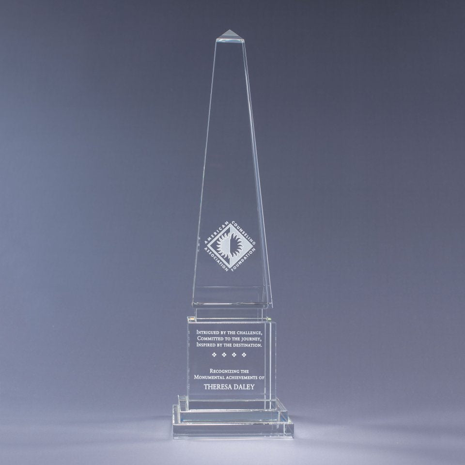 Clear glass obelisk award with Sand etch engraved text and logo on a gray background