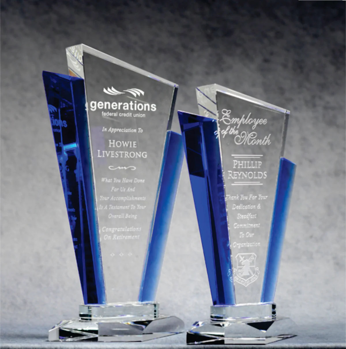 A set of clear crystal awards with blue accents and personalized engravings on the front.