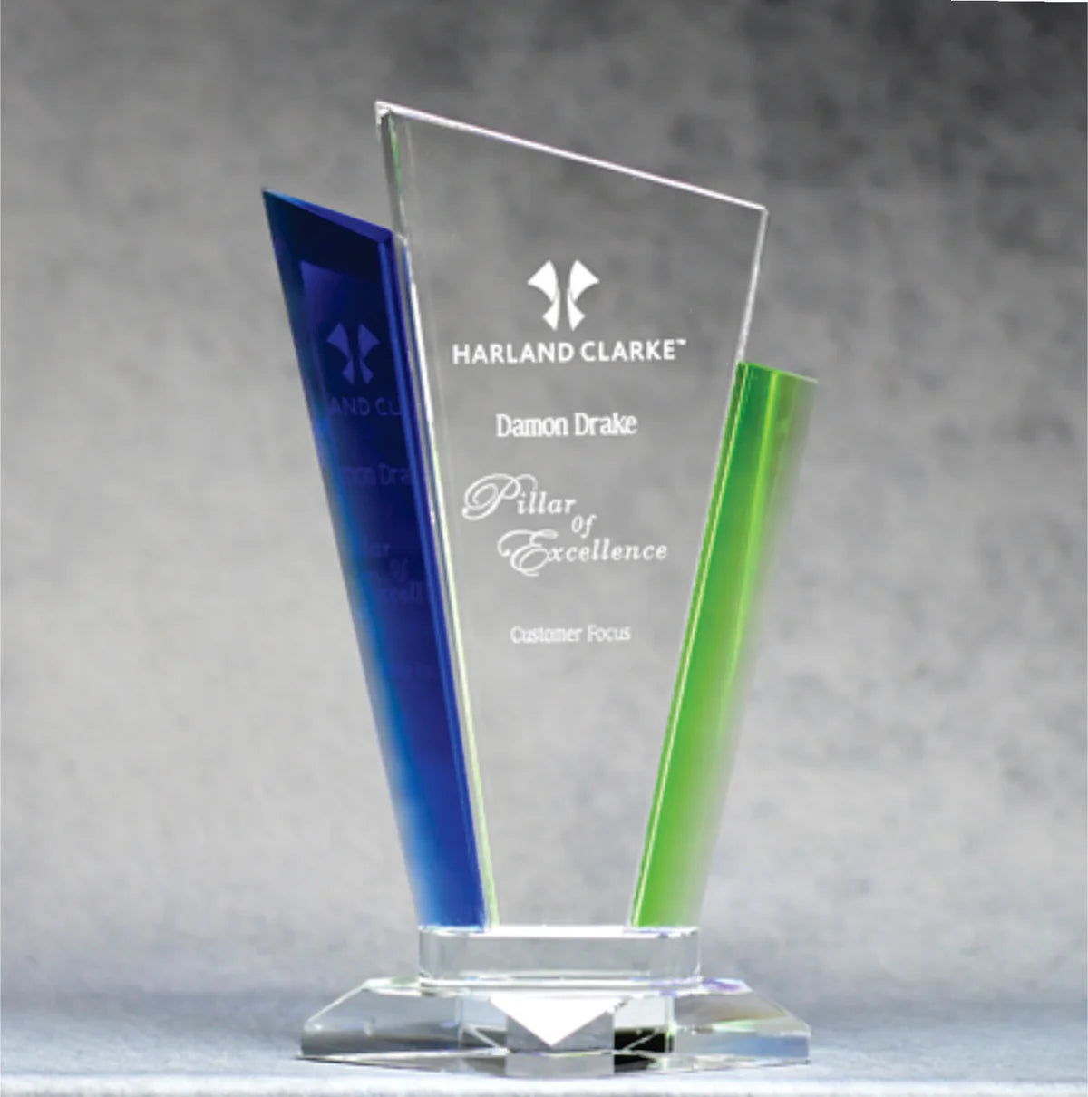 Two optic crystal palace awards with blue and green accents, standing at different angles, displaying engravings on their surfaces.