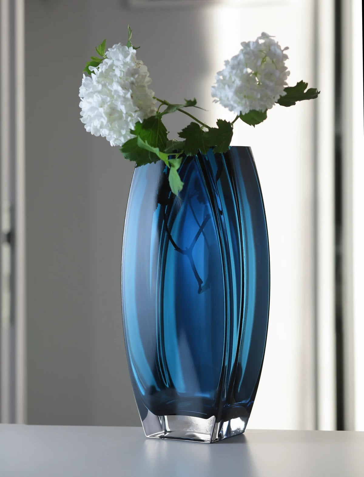 Blue glass vase with white flowers on a neutral background