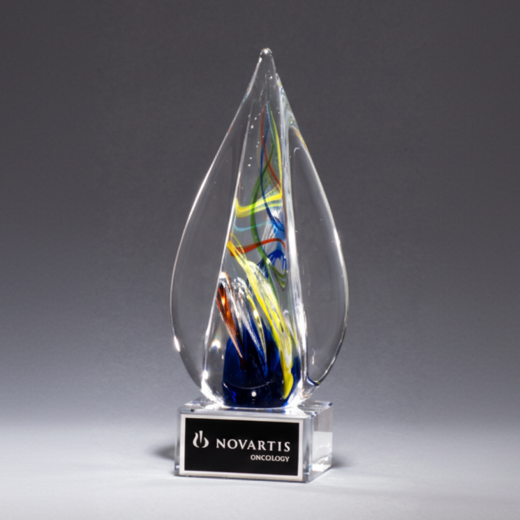 A flame-shaped art glass award with a clear glass base and a laser engraved aluminum plate on the base. The award is multicolored with a striking visual design.