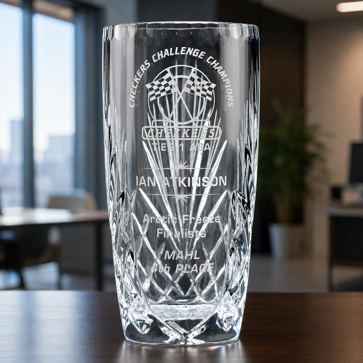 A clear cut-glass trophy cup with etched text and a logo graphic, in an office setting 