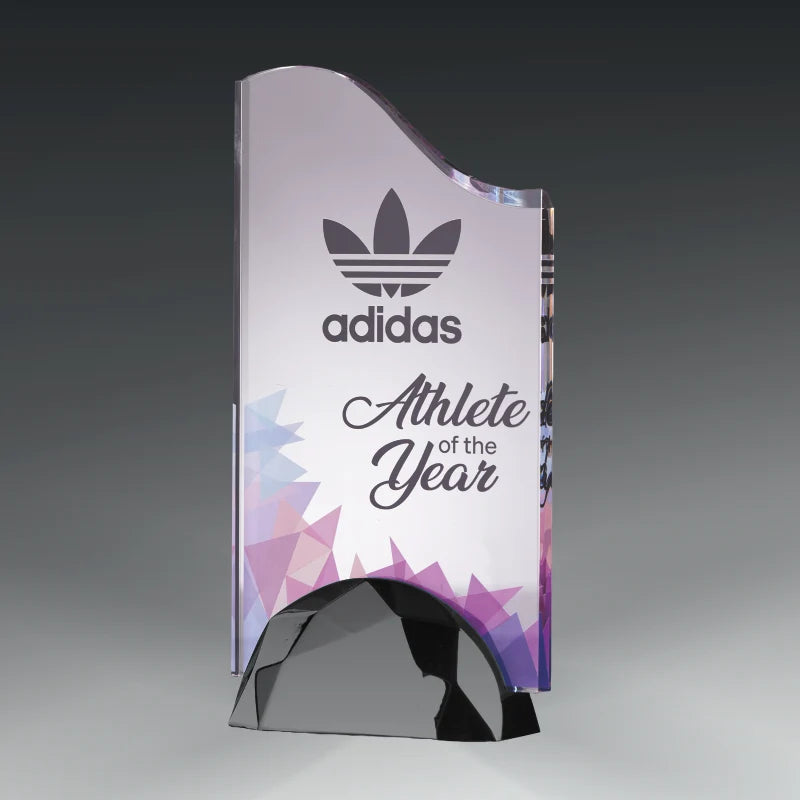 A transparent acrylic award trophy with a curved top and a faceted geometric base, featuring the Adidas logo and the text 'Athlete of the Year' on a gray gradient background.