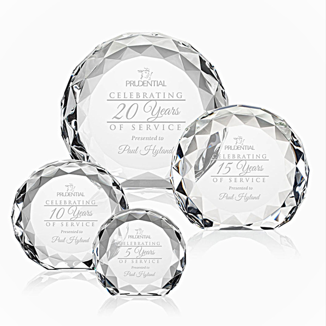 A set of clear crystal awards with faceted surfaces, each engraved with recognition language such as 'Celebriting 20 Years of Service'.