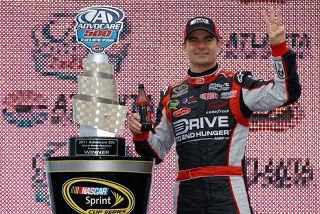 Nascar legend in racing suit holding a winner trophy with a prominent brand logo in the background