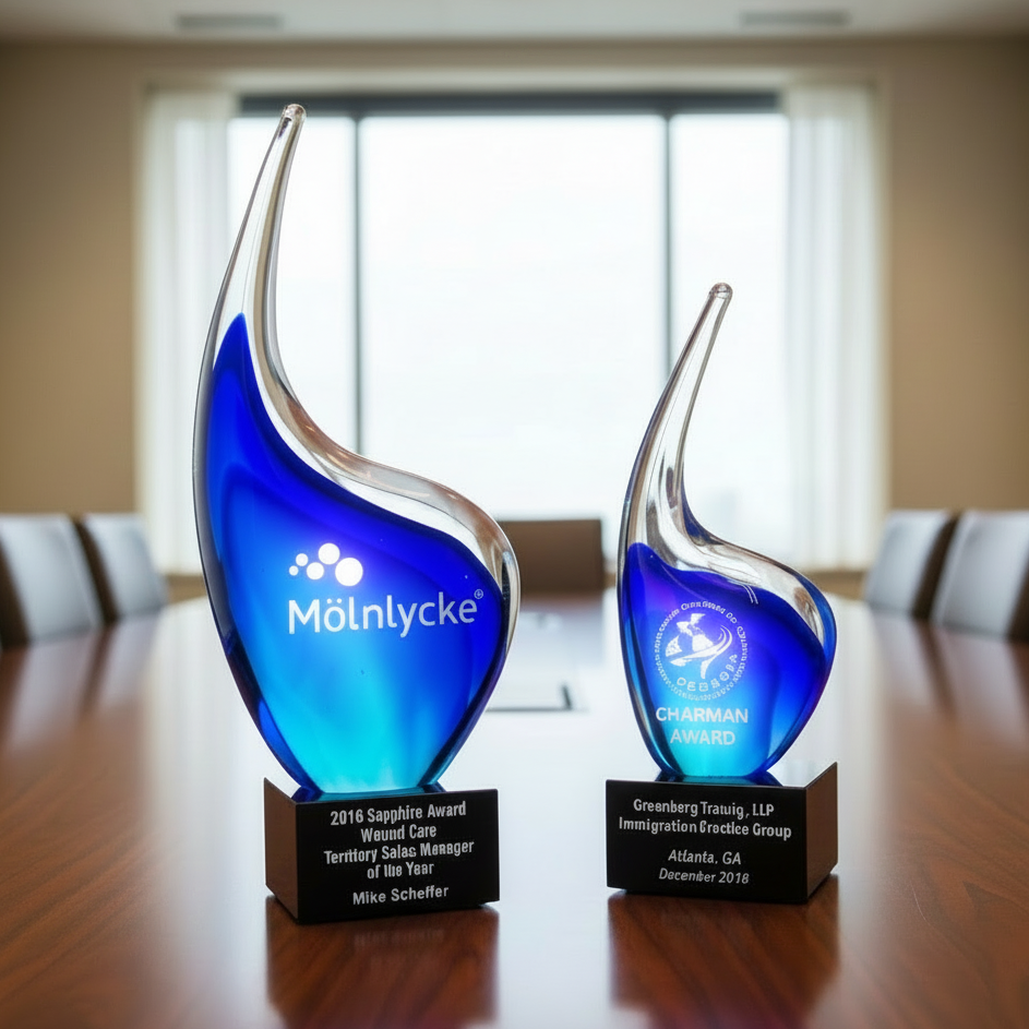 Two blue glass awards on a wooden table in a conference room.