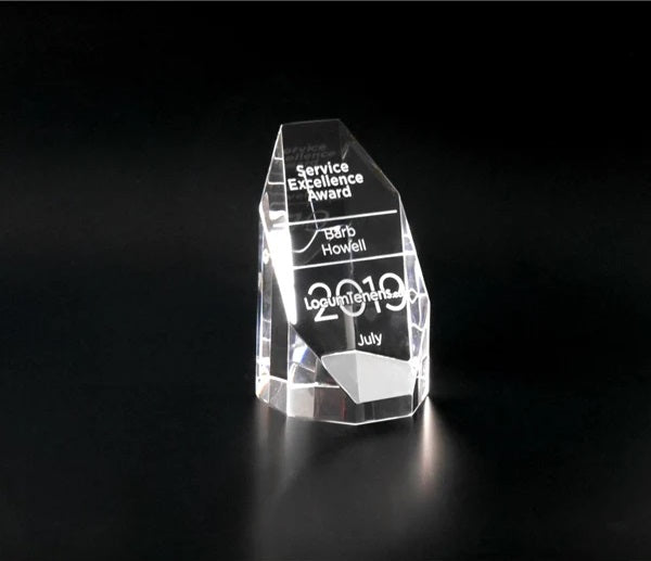  clear crystal silhouette tower awards of varying sizes, with engraved text displayed against a dark background.
