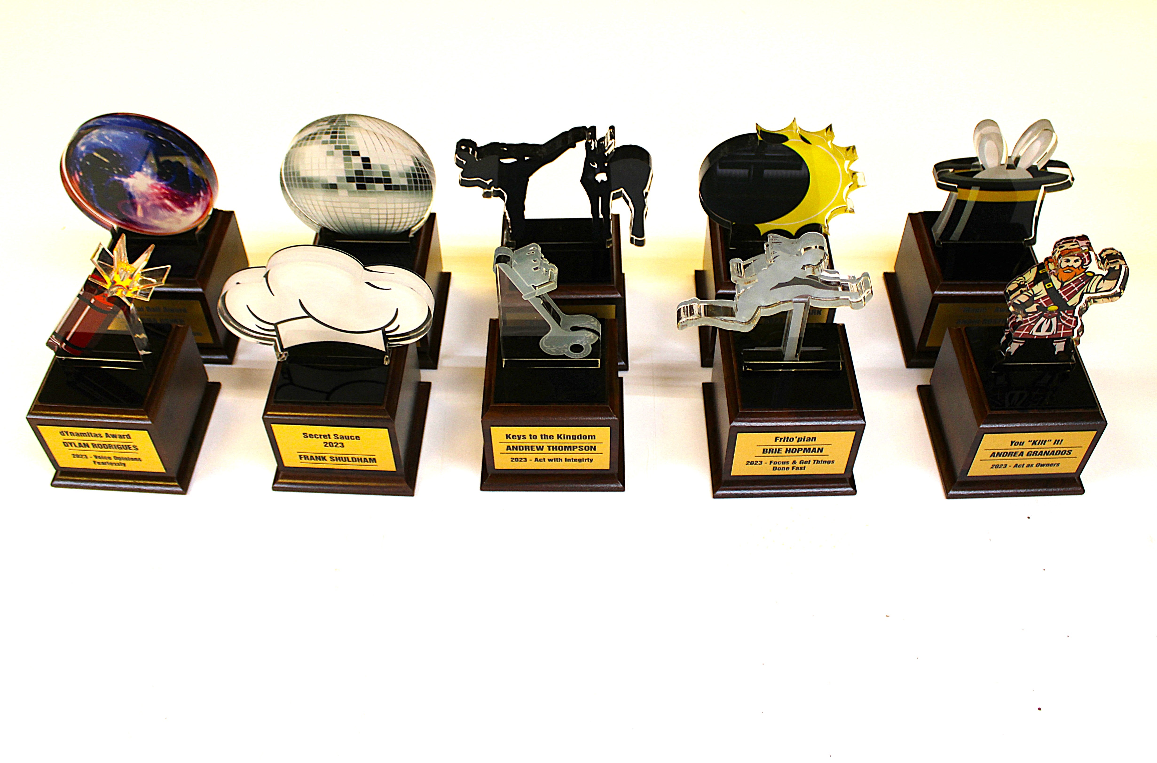 A collection of custom deal toy acrylic awards with various designs, mounted on wood bases. 