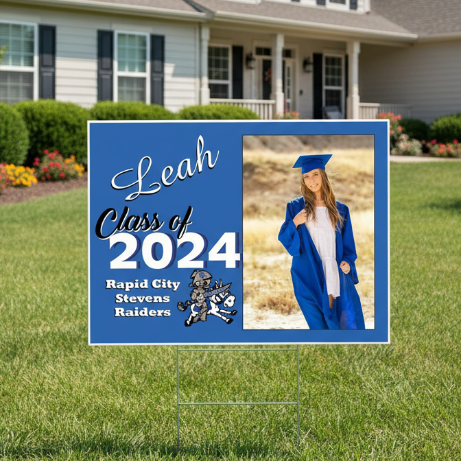 Graduation-themed yard sign with a photo of a graduate in front of a house.